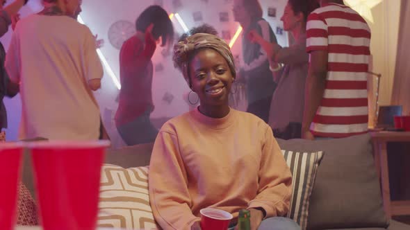 Cheerful Black Woman Posing for Camera on Couch at Home Party with Friends