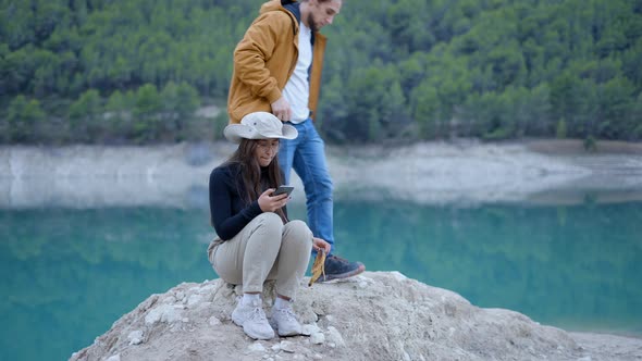 Young Man Sits Down Next to Girl with Phone in Nature and Peels Apple