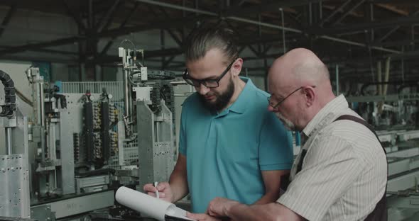 Two Engineers of Industry Stand at Facility, Have Discussion and Use Notebook