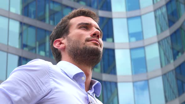 A Businessman Stands in Front of an Office Building and Looks Around Proudly - Closeup From Below