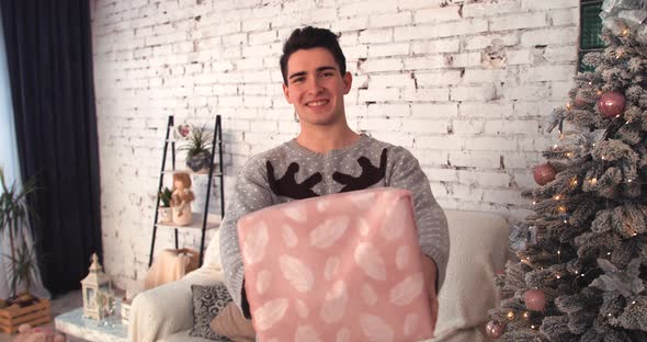 Young Guy Smiling at Christmas Gives a Pink Gift To the Camera