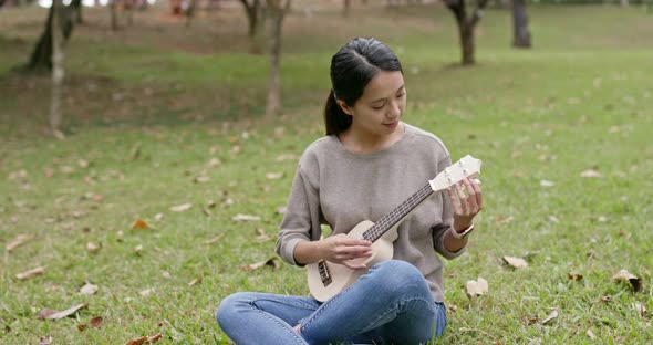 Asian Woman enjoy play ukulele and song in the park