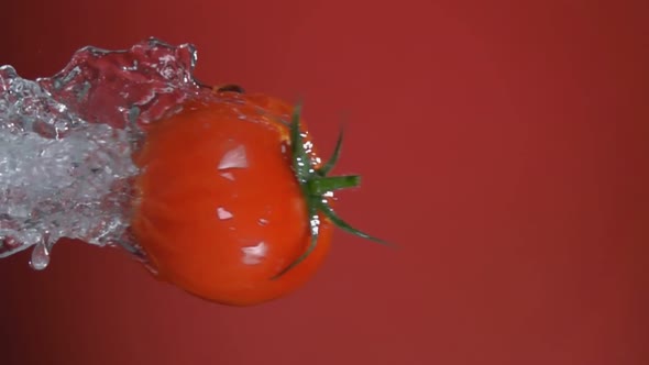 A Wet Red Cherry Tomato is Flying Horizontally on the Red Background
