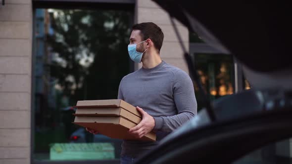 Delivery man wearing mask holding delivery boxes and twists head in search of customer.