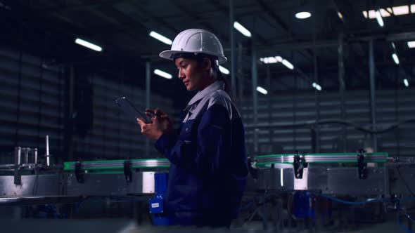 Engineer is using a tablet to check the machine's control system in a factory.