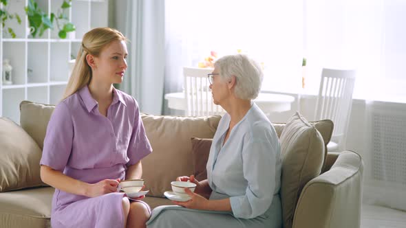 Young daughter and elderly mother drinking tea at home