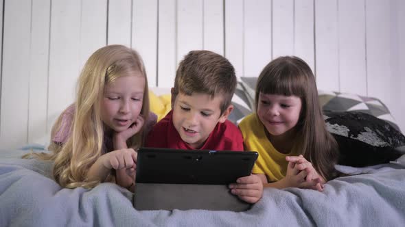 Modern Childhood, Little Friends in Multi Colored T-shirts Use Digital Tablet and Chat While Lying