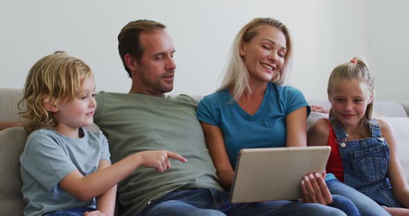 Caucasian parents on sofa with son and daughter talking and looking at digital tablet