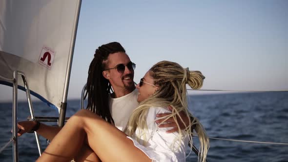 Stylish Couple with Dreadlocks in White Clothes and Sunglasses Sitting Embracing on the Bow of the