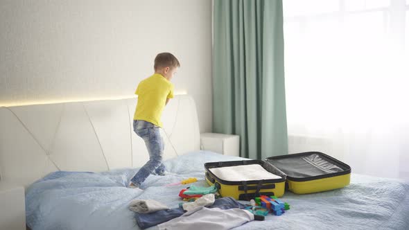 Child Traveller Is Happy and Jumps Around the Travel Suitcase on the Bed