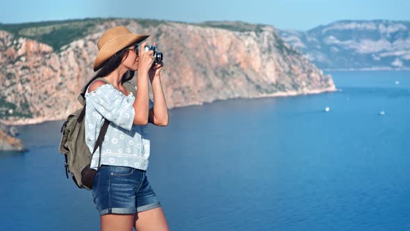 Attractive Travel Woman in Hat and Sunglasses Taking Picture of Seascape Using Camera