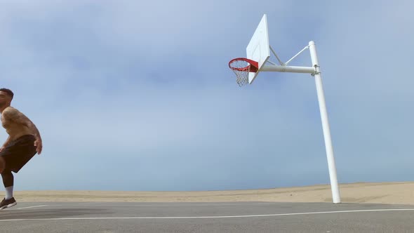 A man takes a layup shot while playing one-on-one basketball hoops on a beach court