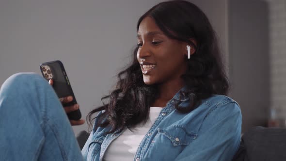 Smiling African woman wearing earbuds looking at phone