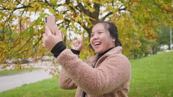 Happy Asian woman taking video call on smartphone at the park in Autumn