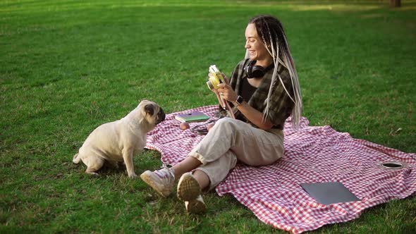 Smiling Girl Taking Photo with Cute Pug Puppy in Green City Park Holding Camera Sitting on Plaid