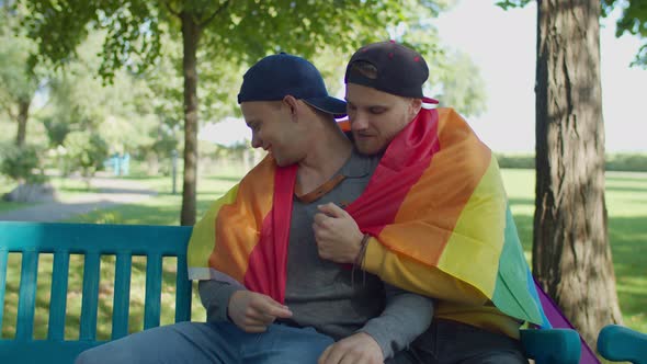 Gay Couple Wrapped in Pride Flag Resting on Bench