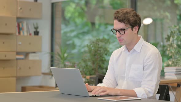 Young Man Feeling Shocked While Using Laptop in Modern Office