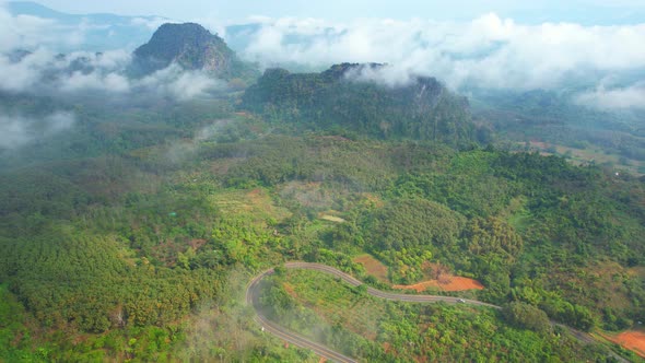 4K Aerial view from a drone flying above rural clouds, road in a tropical forest in Thailand