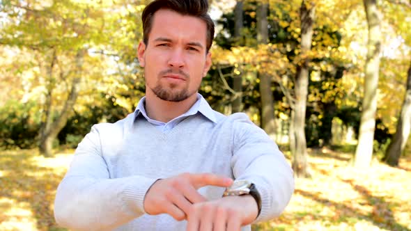 Young Man Stands in the Woods and with a Serious Face Shows on Watch