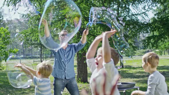 Group of Little Kids Playing with Soap Bubbles at Performance in Park alt