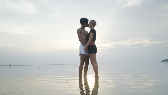 Silhouetted Couple Kissing at Sunset Standing in Shallow Calm Sea Water with Sunlight Reflection on