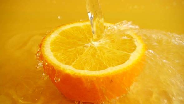 Half of an orange in a jet of water on an orange background. Slow motion.