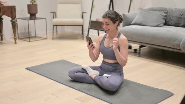 Young Indian Woman Talking on Video Call on Smartphone While Sitting on Yoga Mat