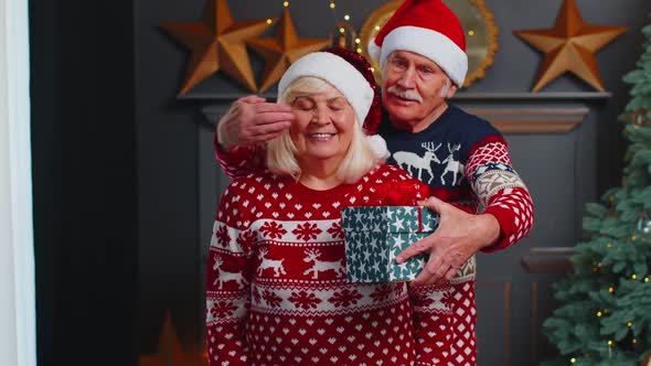 Grandfather Covering Eyes of Old Grandmother with Surprise Christmas Gift Present Box at Home Room