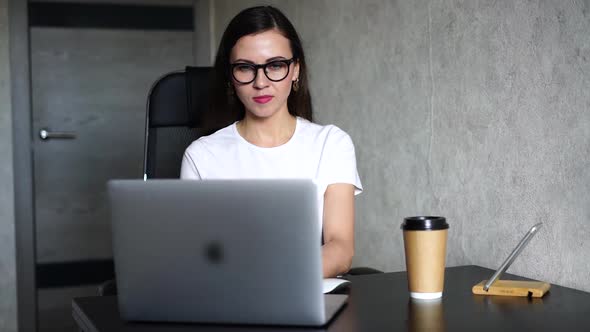 Close-up Portrait of a Woman in Glasses with Long Dark Hair, She Is in the Room, Sitting at a Table