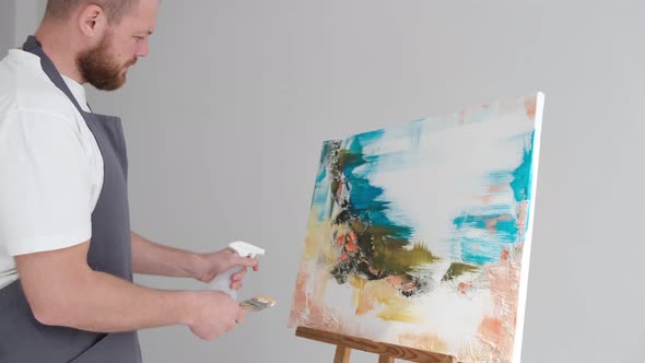 A Talented Man Stands in Front of an Easel and Paints an Abstract Picture