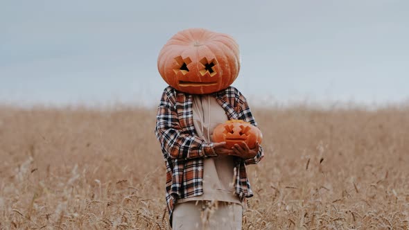 A Funny Woman in a Shirt with a Big Pumpkin Head Holds a Small Pumpkin in Her Hands Dancing Outdoors