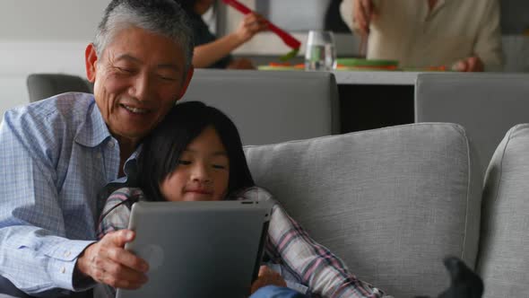Front view of cute asian granddaughter and old senior grandfather using digital tablet at home 4k