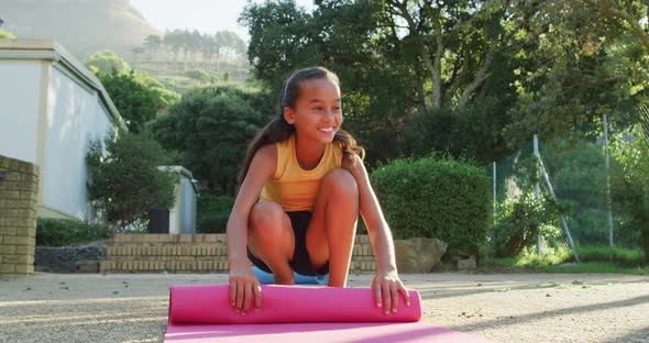 Mixed race schoolgirl rolling mat after yoga lesson outdoors