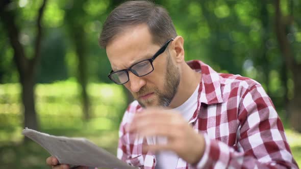 Aging Man in Eyeglasses Trying to Read Newspaper in Park