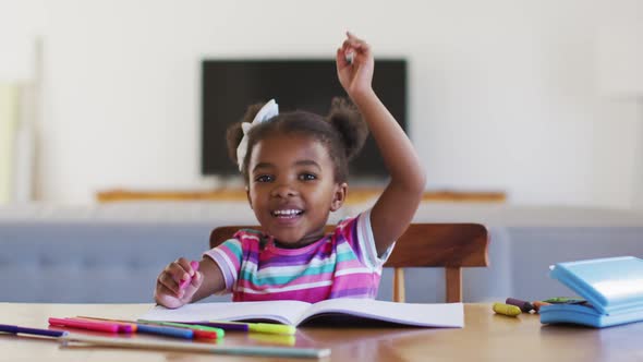 Happy african american girl raising hand during online school at home