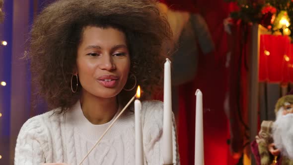 Charming African American Woman in a White Sweater Lights White Holiday Candles