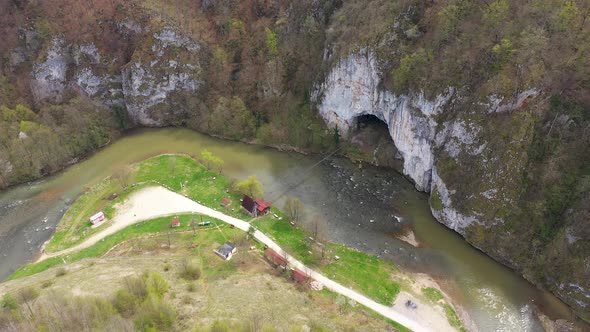 Aerial Above View of a Wild Mountain River Meander and a Gigantic Cave Entrance
