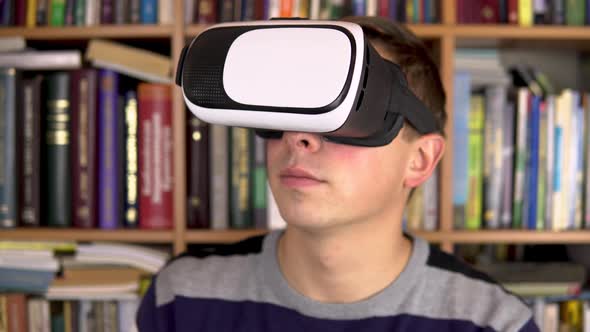 Young Man in VR Glasses in the Library. A Man with a VR Helmet on His Head Examines and Touches
