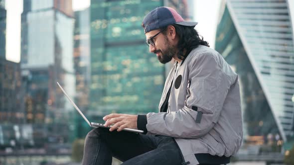 Handsome Young Man Sitting on the Street at the Business Center with a Laptop