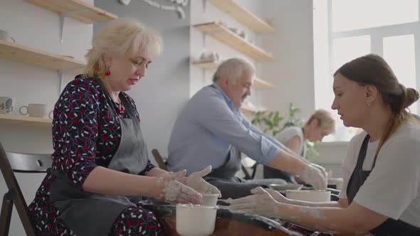 Medium Shot of Middle Aged Ceramic Artist Teaching Group Elderly Caucasian Woman and Senior Man How