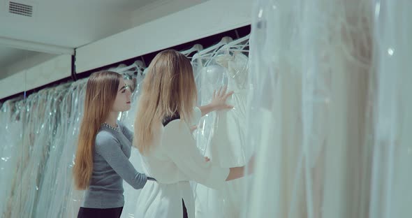 Happy Girlfriends Look at Wedding Dresses, Choose the Size. Happy Bride Is Preparing for the Wedding