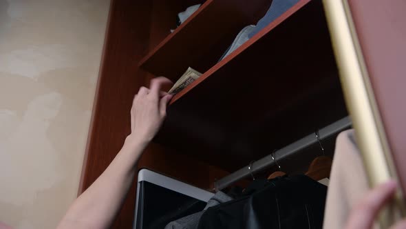 girl opens the cabinet door and hides a small stack of money on the top shelf