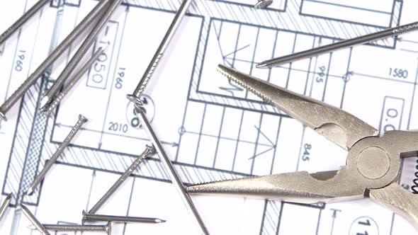 Gray and Yellow Round-nose Pliers on Building Plan, Scheme Among Nails, Rotation, Close Up