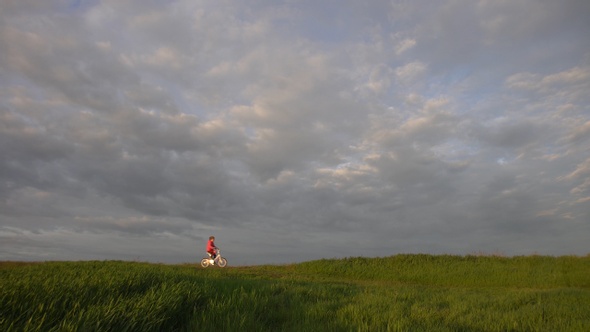 Little girl rides a bicycle rides on a scenic rural road at sunset