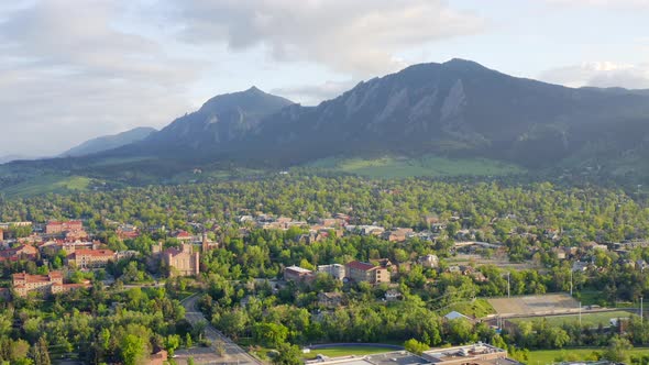 Aerial pan left of beautiful flatiron mountain vista, bright green trees, and CU Boulder campus in B