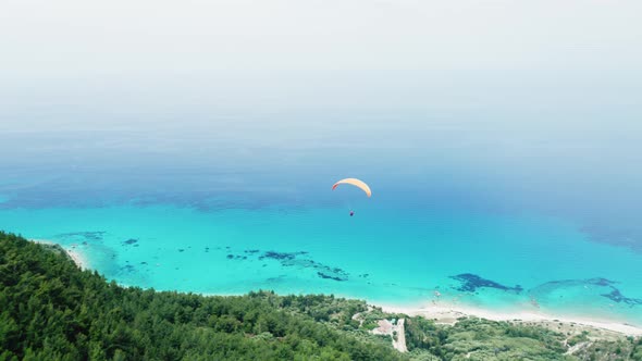 Drone view of paragliding over scenic hill and coastline.