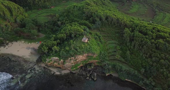 Aerial top down shot showing old building on hilltop with cliff,ocean and private sandy beach