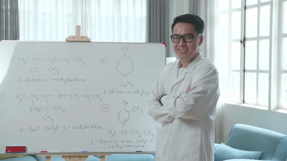 Asian Male Teacher With Glasses Crossing Arms And Smiling To Camera While Teaching Chemist At Home