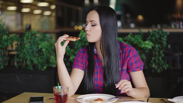 beautiful girl in a plaid shirt is eating a slice of pizza at a table in the pizzeria