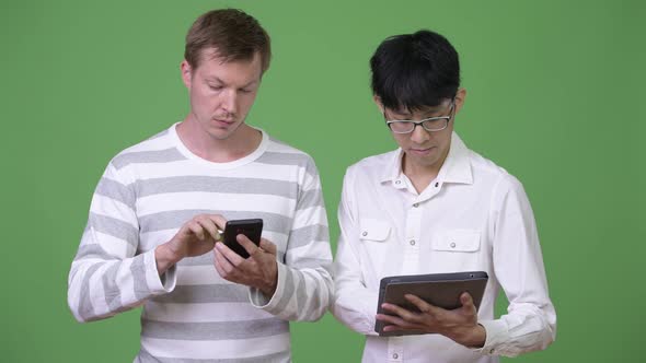 Two Young Multi-ethnic Businessmen Using Phone and Digital Tablet for Social Media Concept